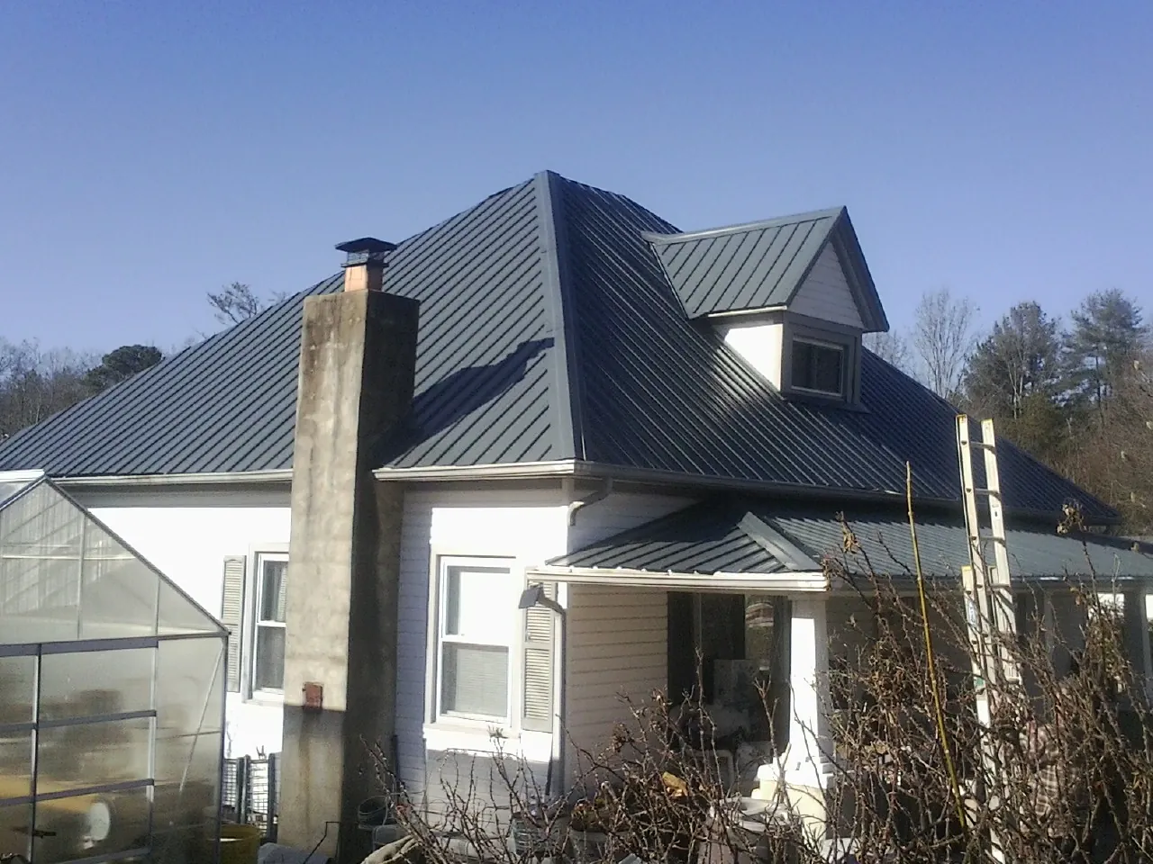 Dark blue standing seam metal roof on a white farmhouse with dormer — Slate & Tile Roof Repair by Roofing Brothers in Boling