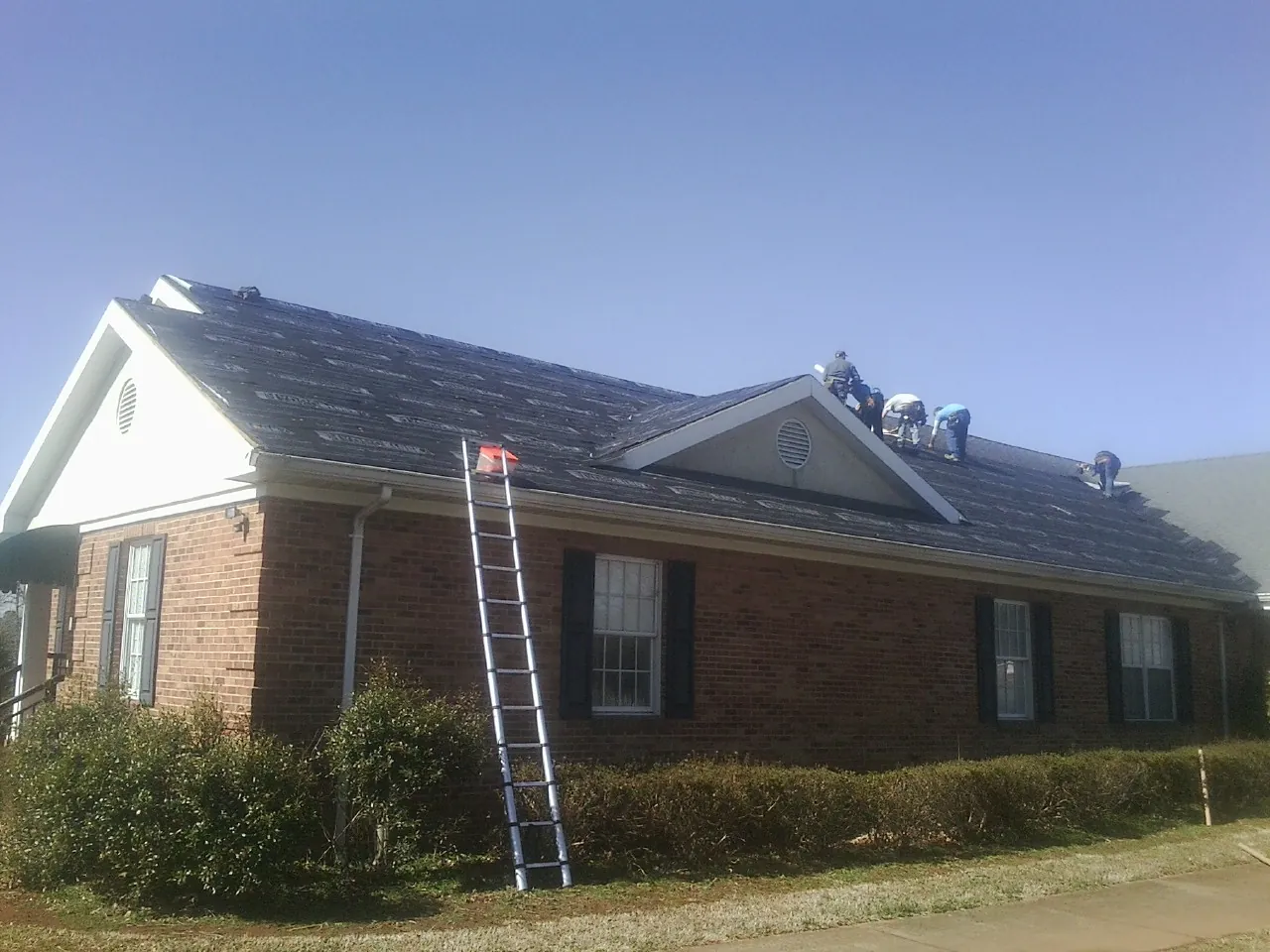 Crew tearing shingles off a brick ranch roof with a ladder set — Metal Roof Repair work by our crew in Boling