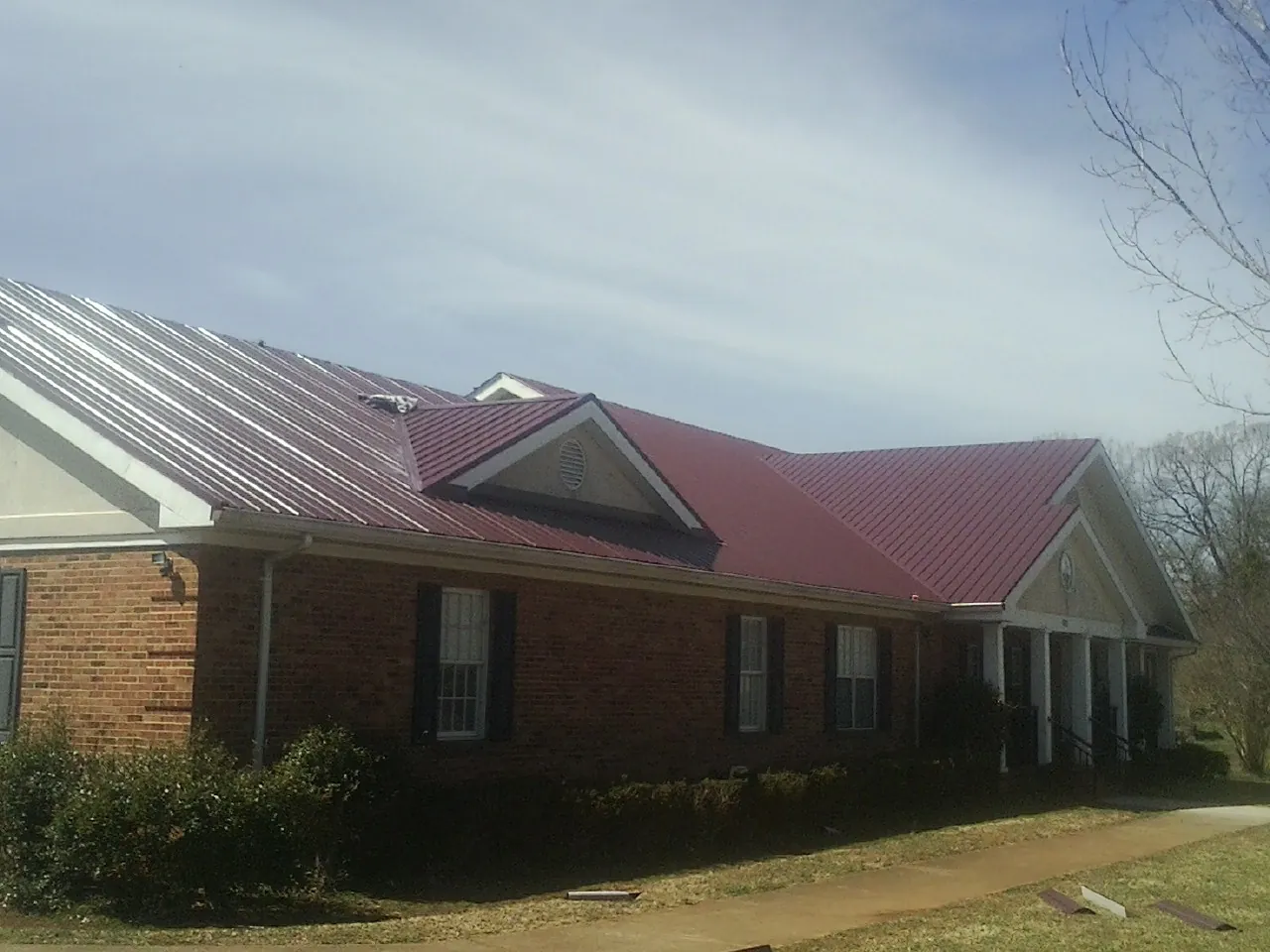 Red metal roof with gabled entries on a long brick building, from a Hail Damage Roof Repair job in Boling