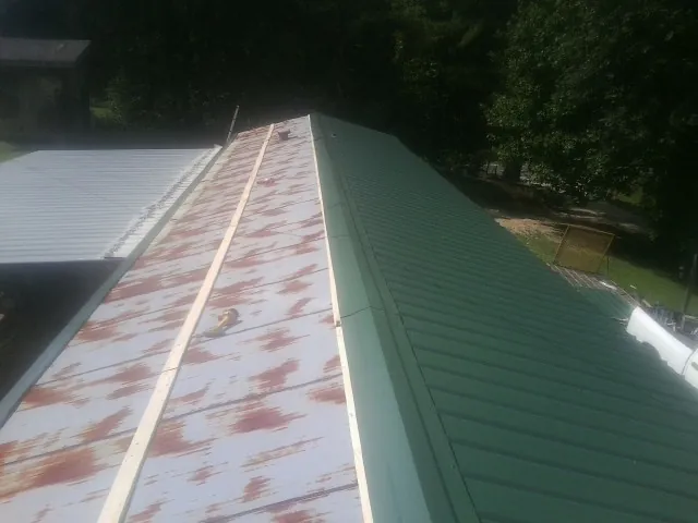 Old rusted panels beside newly installed green metal roofing — Wind Damage Roof Repair by Roofing Brothers in Boling