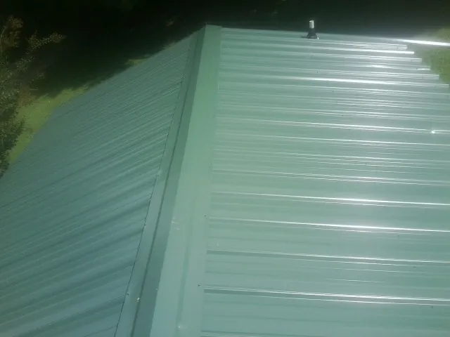 New green metal panels meeting at the ridge of a roof — Flat Roof Repair work by our crew in Boling