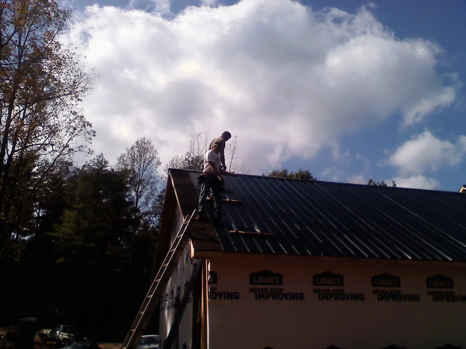 Roofer fastening dark metal panels high against a cloudy sky, from a Roof Inspection job in Boling
