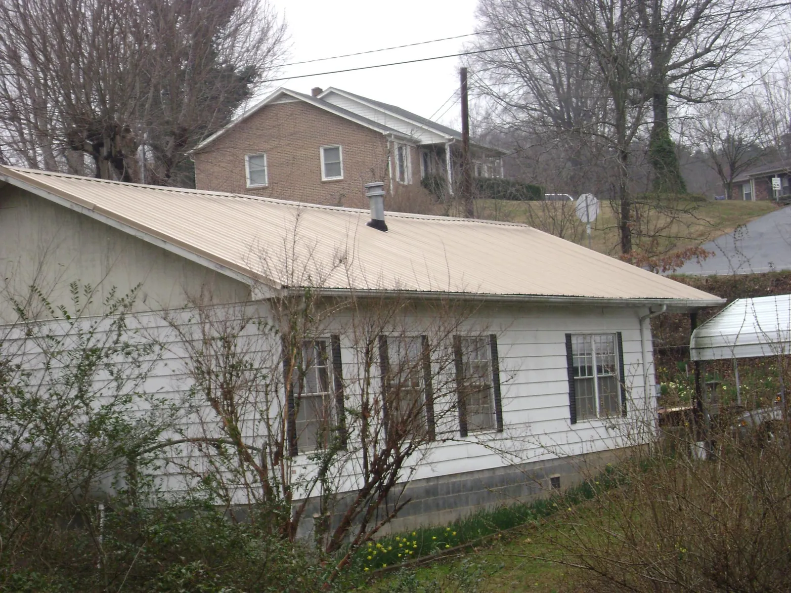 Tan metal roof on a white sided house set into a hillside — Commercial Roofing by Roofing Brothers in Boling