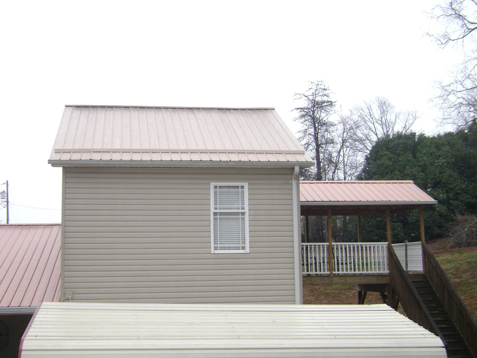 Tan metal roofs on a two story addition and attached porch, from a Roof Replacement job in Boling